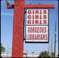 Daytime photograph of a seedy roadside neon sign saying "GIRLS GIRLS GIRLS. GORGEOUS LIBRARIANS."